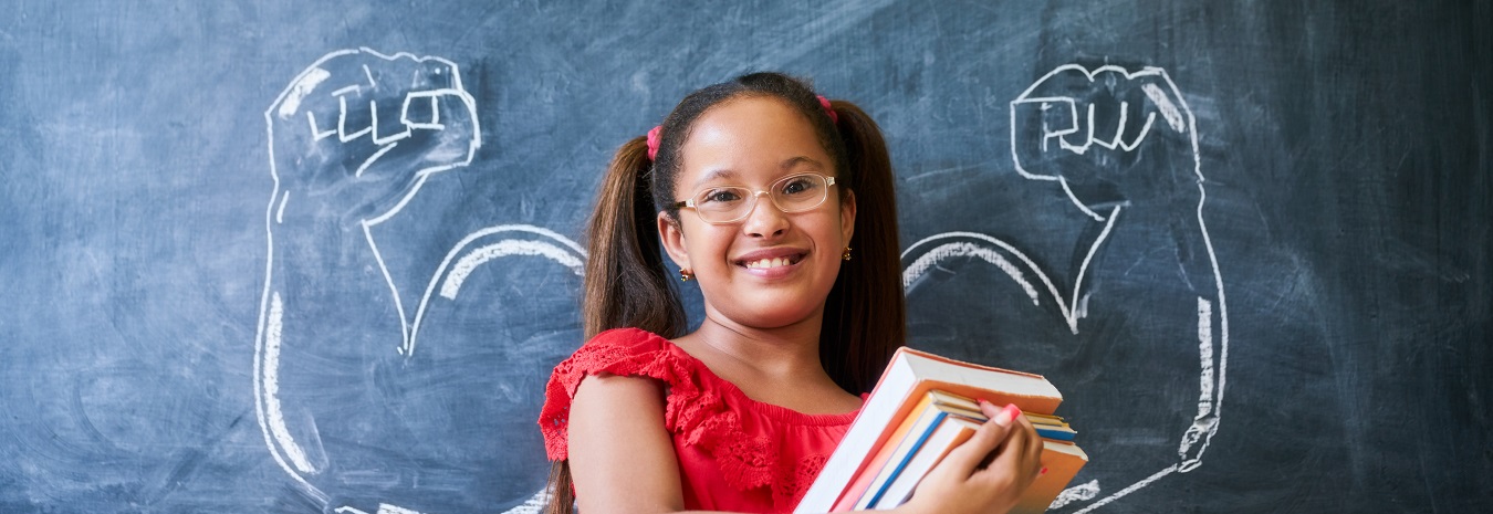 Hispanic Girl Holding Books In Classroom And Smiling